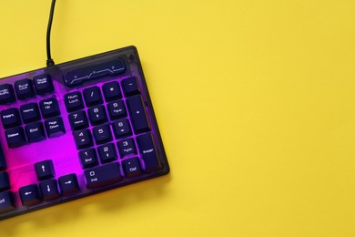 Photo of Modern RGB keyboard on yellow background, top view. Space for text