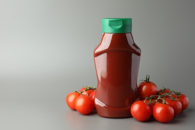 Bottle of tasty ketchup and tomatoes on light grey background. Space for text