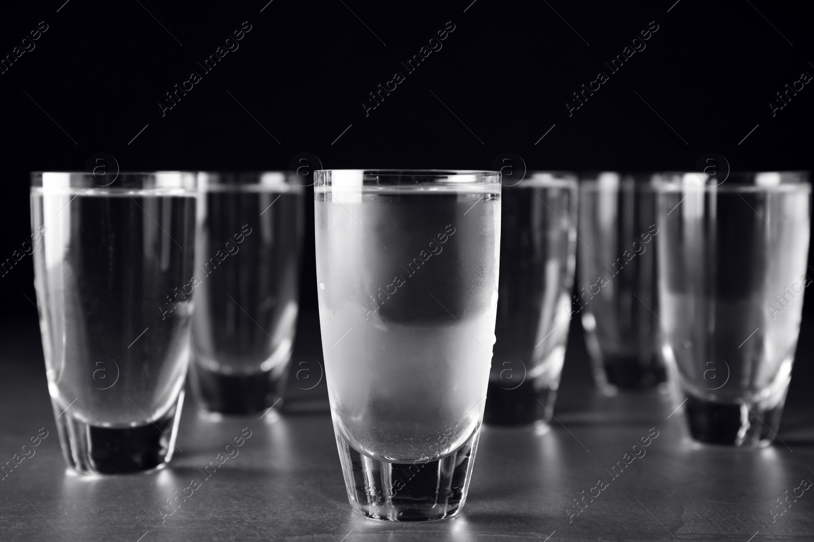 Photo of Shots of vodka on grey table against black background