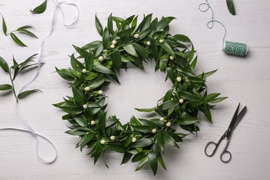 Photo of Beautiful handmade mistletoe wreath and florist supplies on white wooden table, flat lay. Traditional Christmas decor