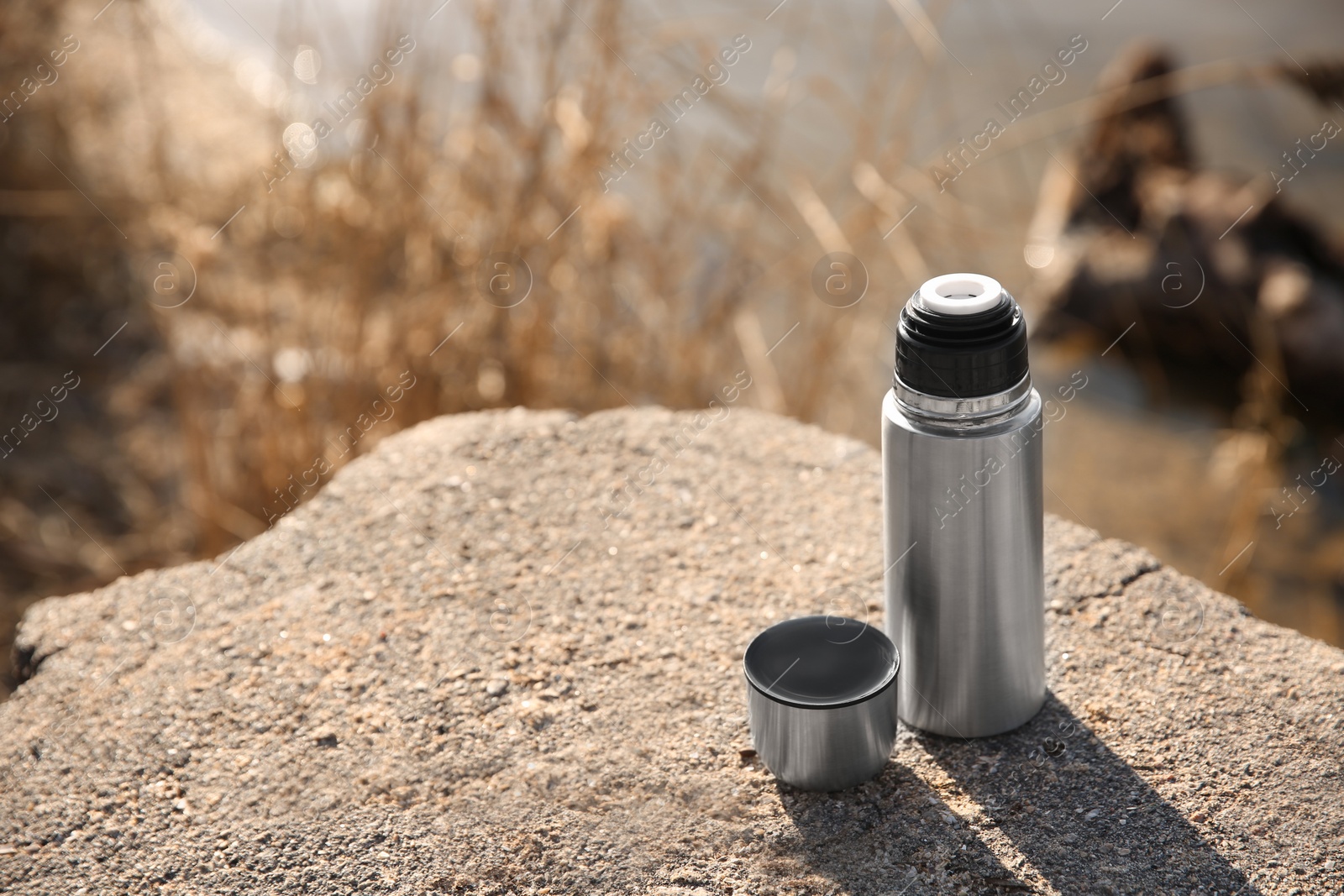 Photo of Modern silver thermos on stone near river