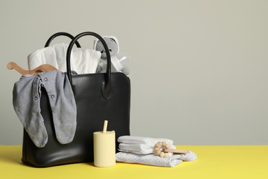 Photo of Mother's bag with baby's stuff on yellow surface against grey background. Space for text