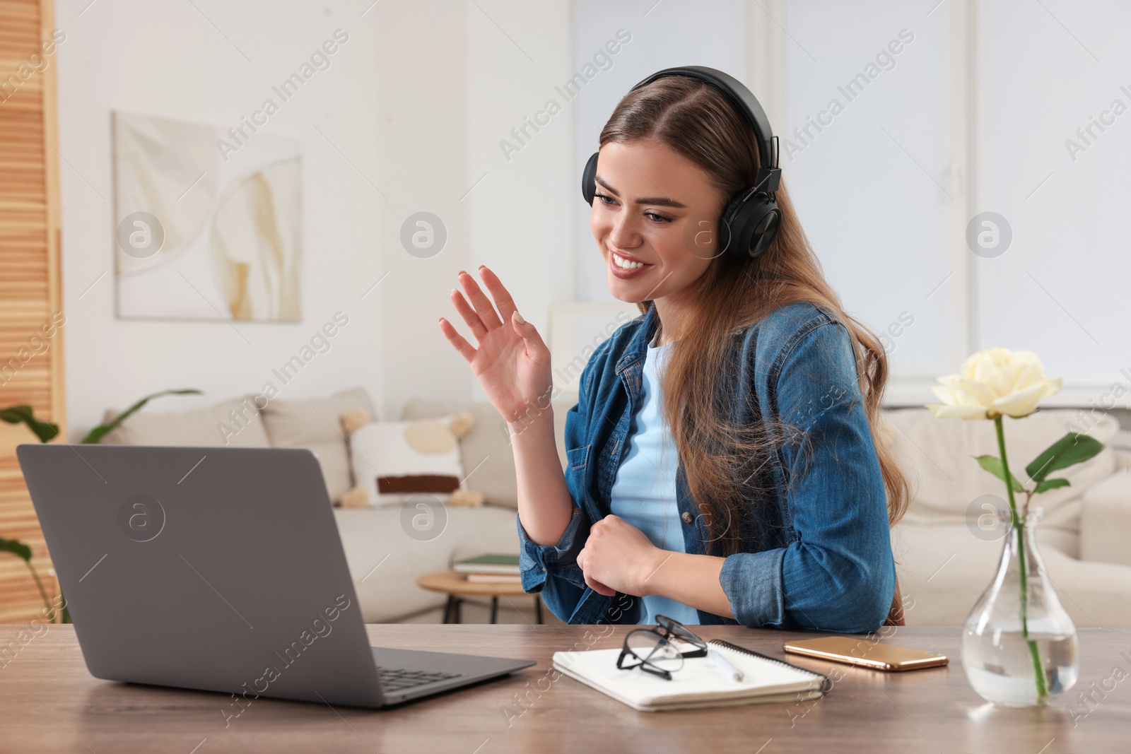 Photo of Happy woman with headphones having video chat via laptop at wooden table