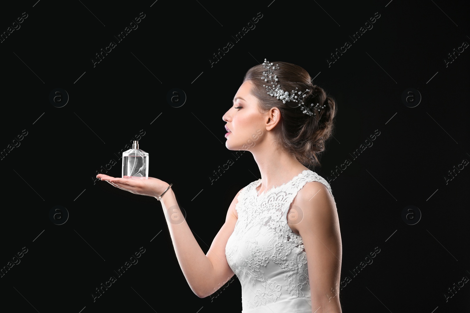 Photo of Beautiful young bride with bottle of perfume on black background