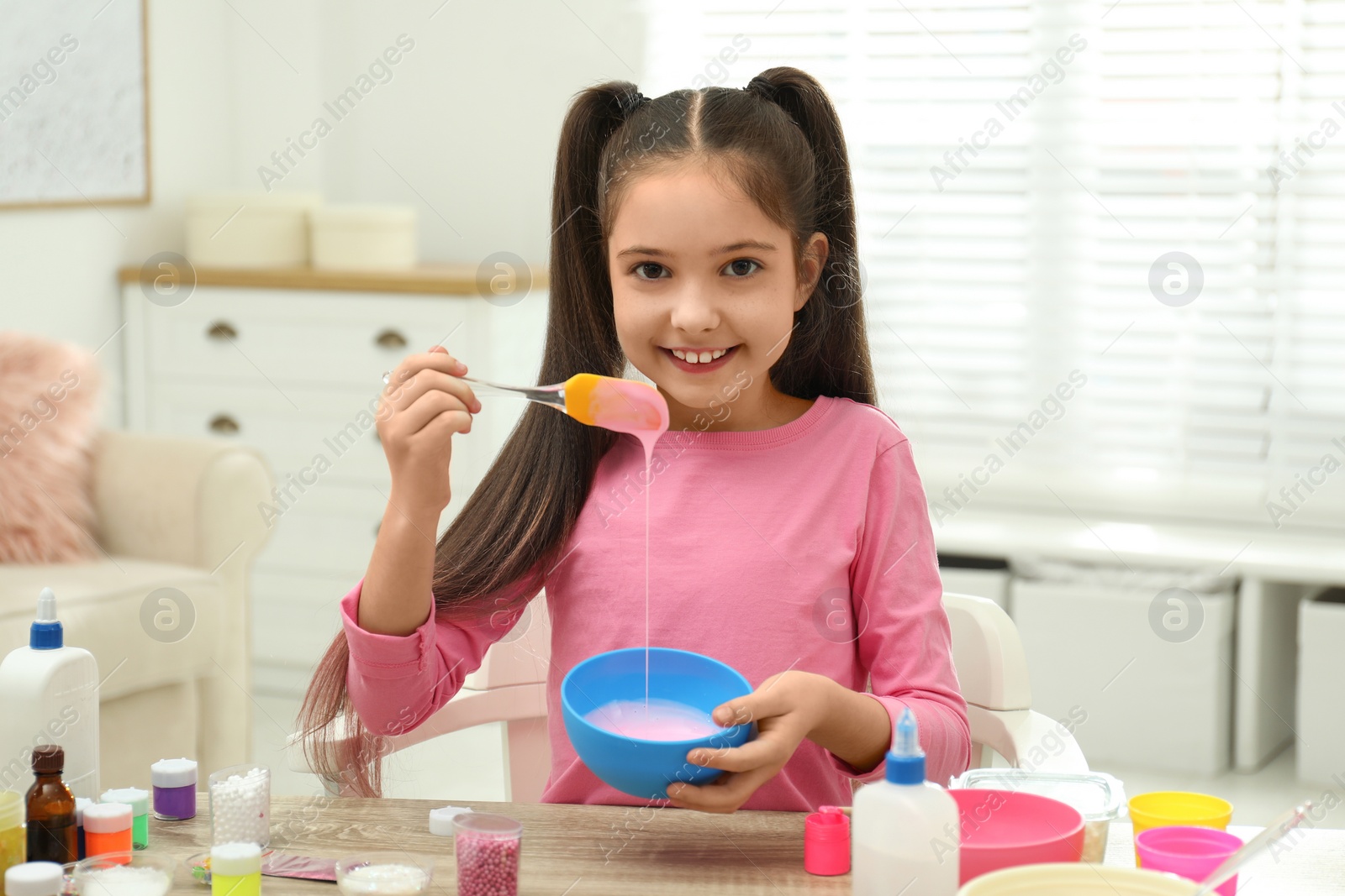 Photo of Cute little girl mixing ingredients with silicone spatula at table. DIY slime toy