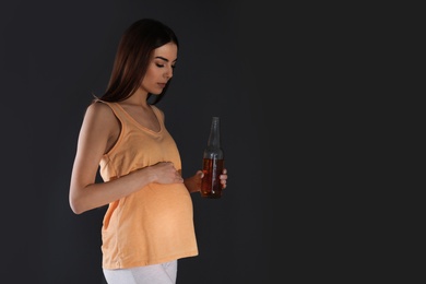 Photo of Future mother with bottle of alcohol drink on black background. Bad habits during pregnancy