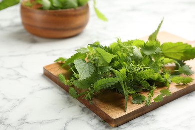 Photo of Wooden board with fresh stinging nettle leaves on white marble table