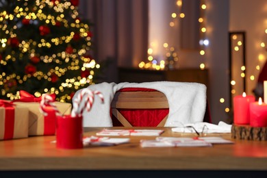 Photo of Santa's Claus workplace. Gift boxes, letters, candy canes on table and costume in room with Christmas tree