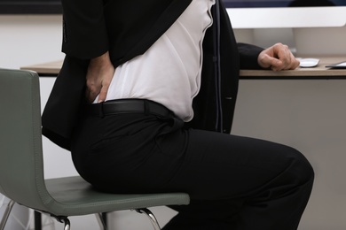 Photo of Businessman suffering from back pain at workplace, closeup