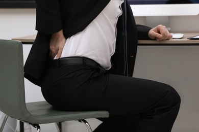 Businessman suffering from back pain at workplace, closeup