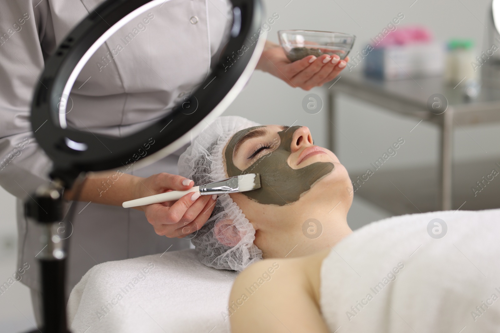 Photo of Cosmetologist applying mask on woman's face in clinic, closeup