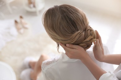 Photo of Professional stylist making wedding hairstyle for bride in salon, back view
