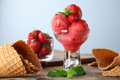 Photo of Delicious strawberry ice cream in dessert bowl on wooden table against light background