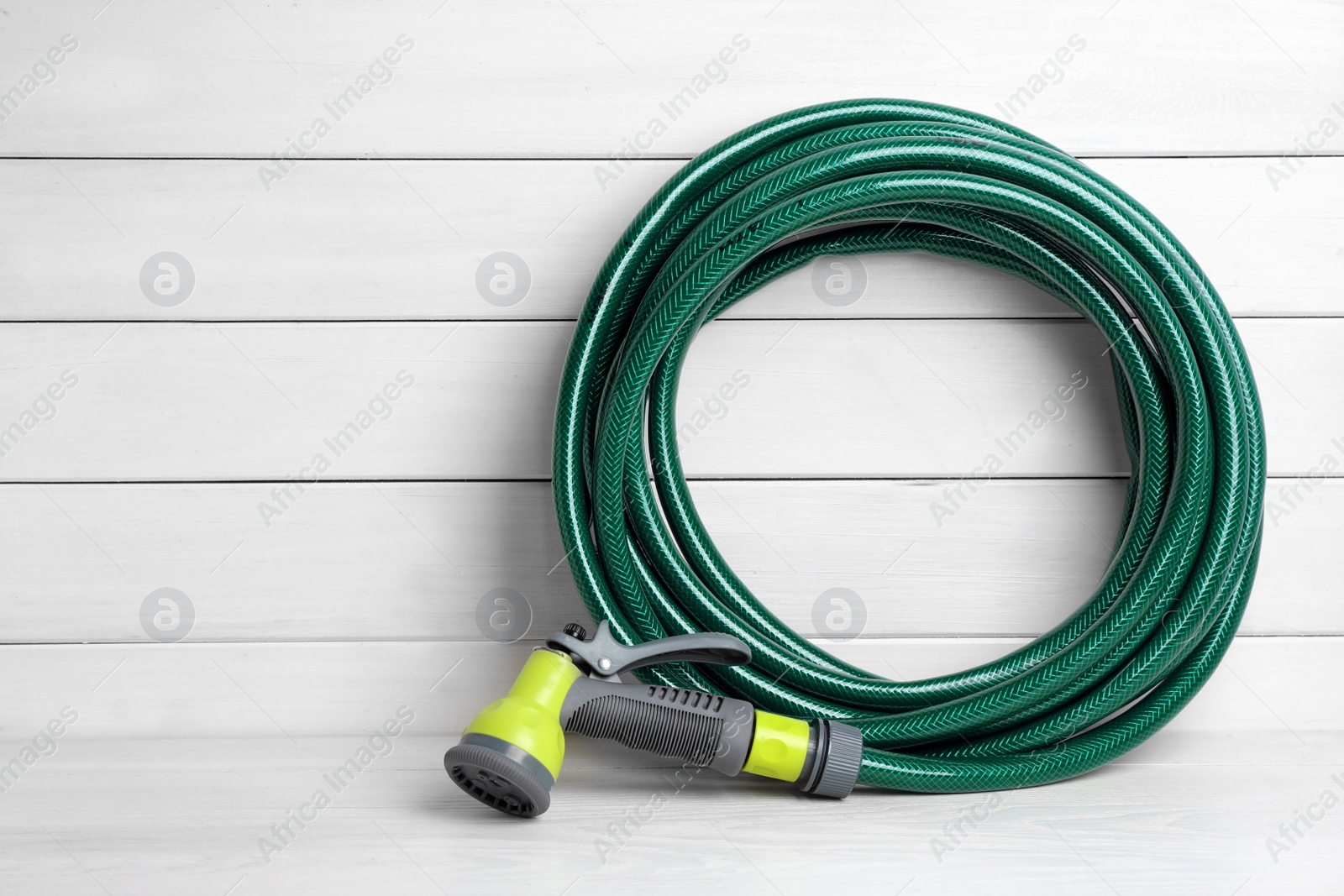 Photo of Green garden hose with spray gun on white wooden table, space for text