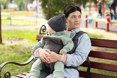 Mother holding her child in sling (baby carrier) on bench in park