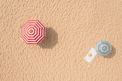 Striped beach umbrellas, towel, hat and flip flops on sandy coast, aerial view