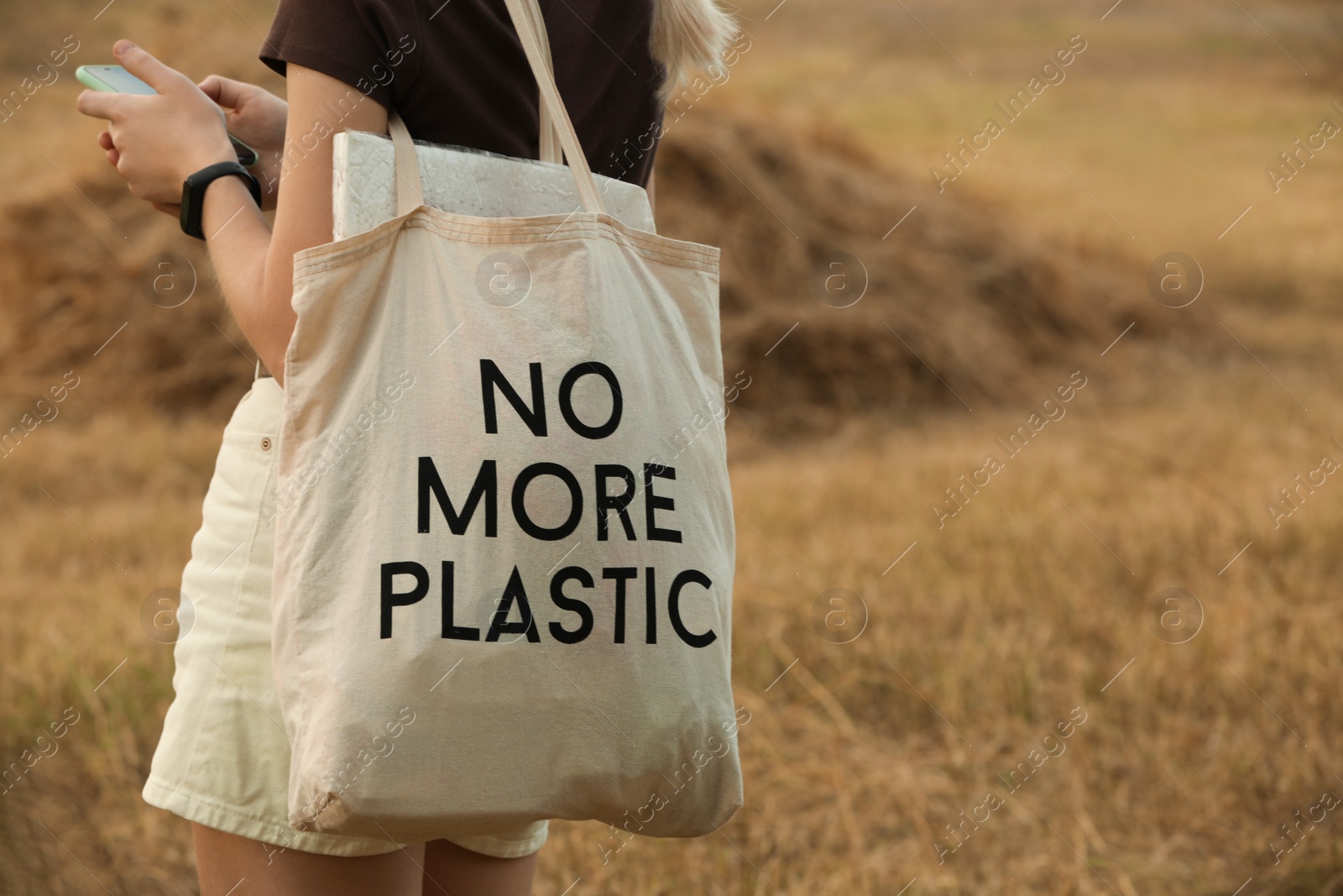 Photo of Woman with smartphone and bag No More Plastic outdoors, closeup. Space for text