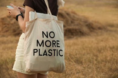 Photo of Woman with smartphone and bag No More Plastic outdoors, closeup. Space for text