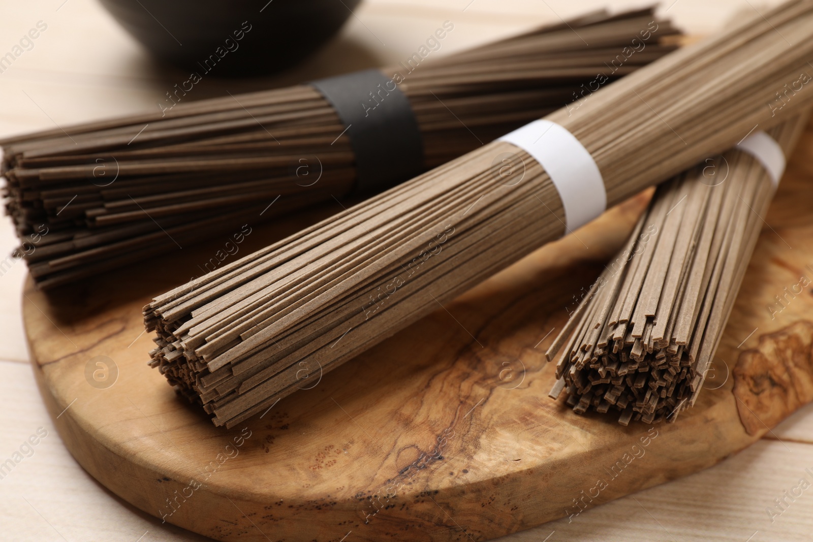 Photo of Uncooked buckwheat noodles (soba) on light wooden table, closeup
