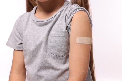 Girl with sticking plaster on arm after vaccination against white background, closeup