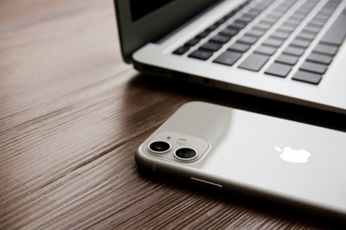 Photo of MYKOLAIV, UKRAINE - JULY 20, 2020: iPhone 11 and MacBook on wooden table, closeup