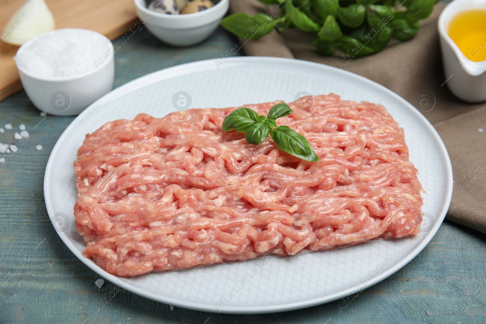Photo of Raw chicken minced meat with basil on light blue wooden table, closeup