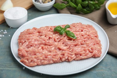 Raw chicken minced meat with basil on light blue wooden table, closeup