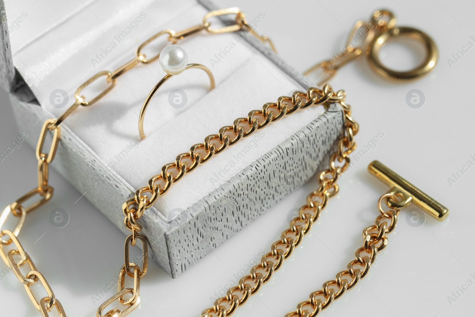 Photo of Metal chain and jewelry box with ring on white table, closeup