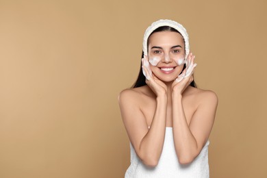 Photo of Happy young woman washing face with cosmetic product on beige background, space for text