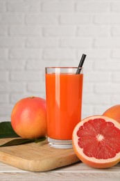 Photo of Tasty grapefruit juice in glass and fresh fruits on light wooden table