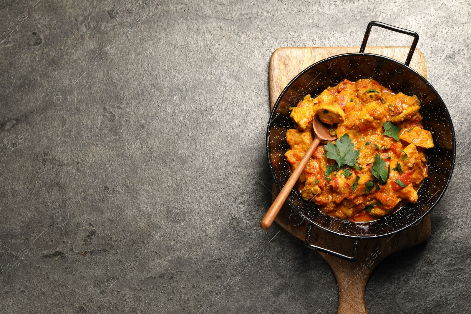 Photo of Delicious chicken curry in frying pan and spoon on grey table, top view. Space for text