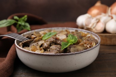 Photo of Delicious fried chicken liver with onion and basil in bowl on wooden table, closeup