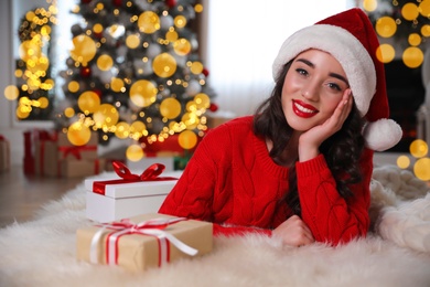 Beautiful woman wearing Santa hat with Christmas gifts on floor at home