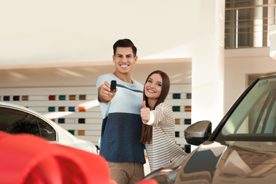 Photo of Happy couple with car key in modern auto dealership