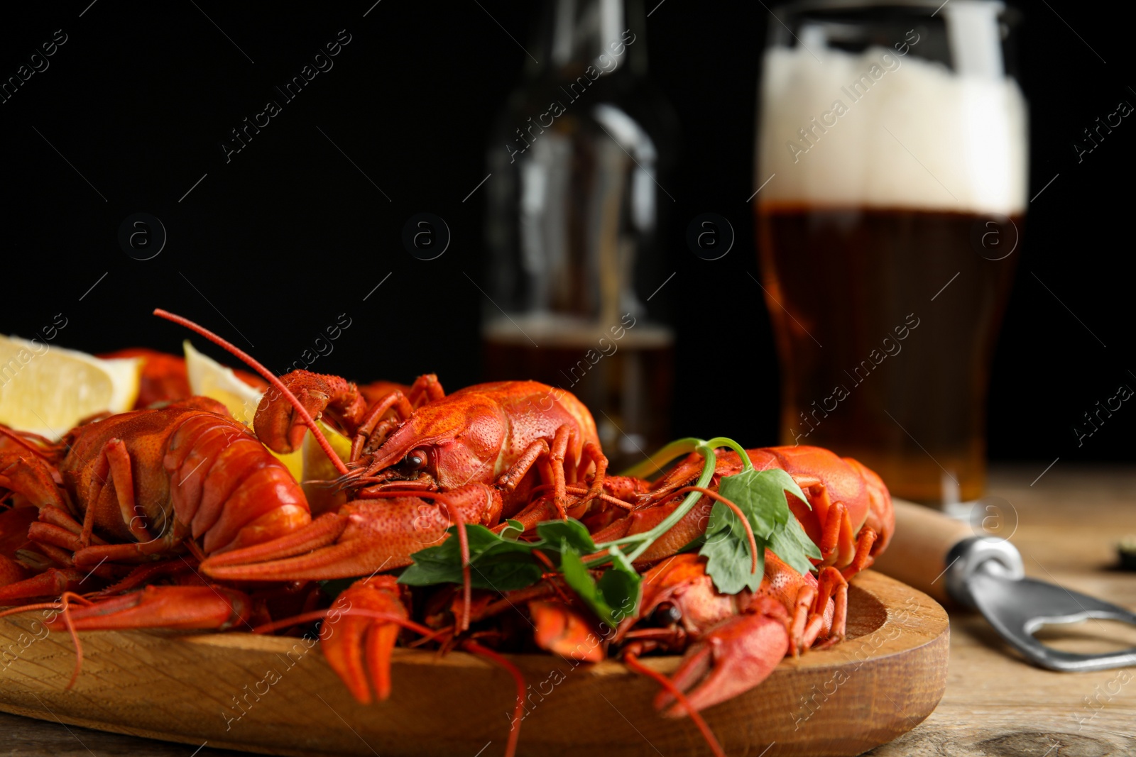 Photo of Delicious red boiled crayfishes and beer on wooden table, closeup