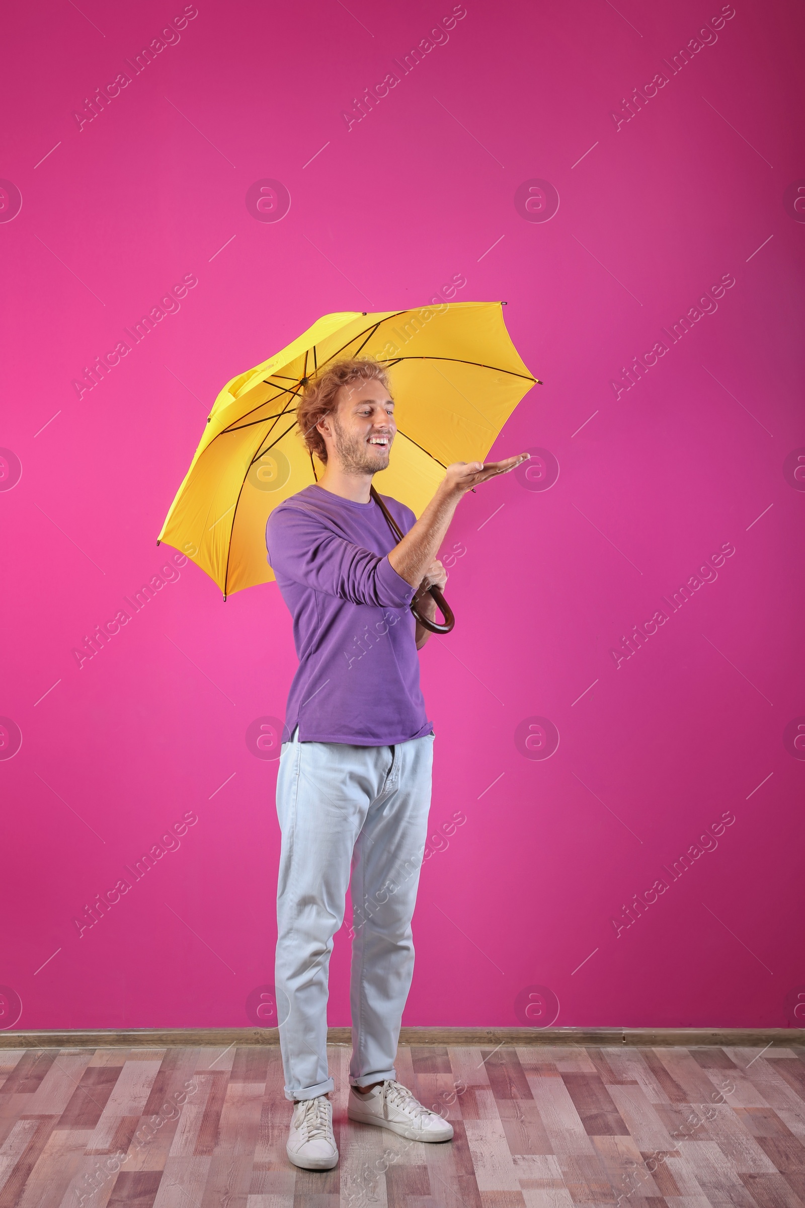 Photo of Man with yellow umbrella near color wall