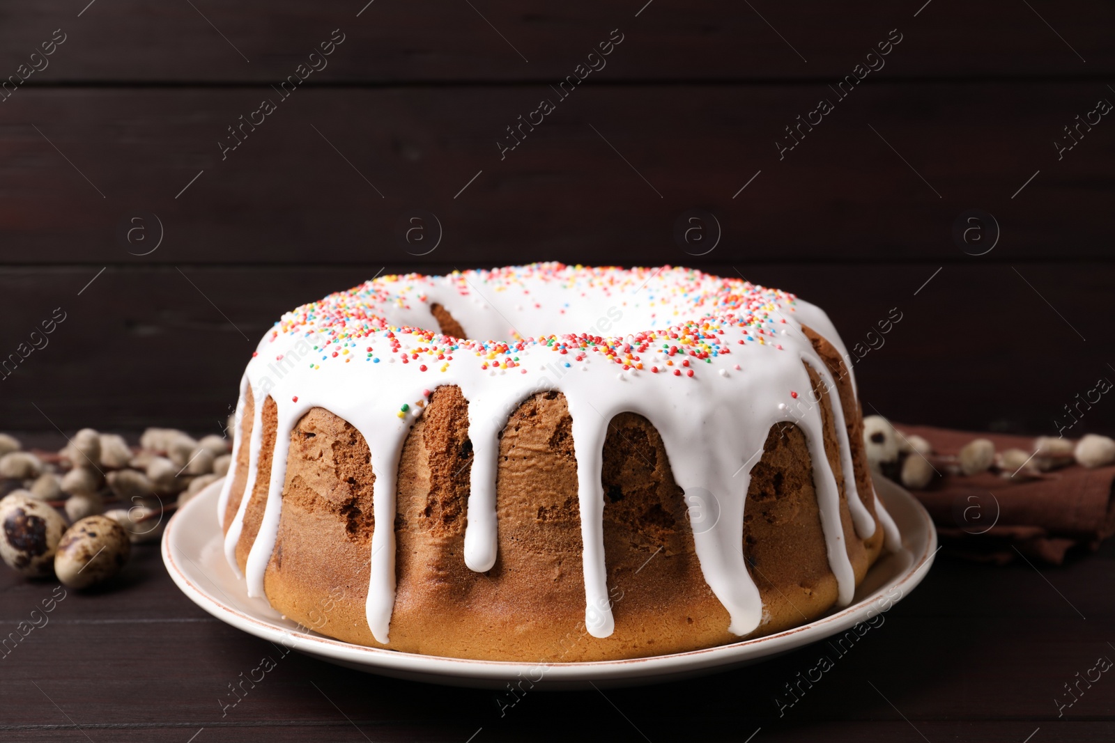 Photo of Glazed Easter cake with sprinkles, quail eggs and willow branches on wooden table