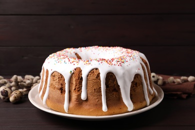 Photo of Glazed Easter cake with sprinkles, quail eggs and willow branches on wooden table