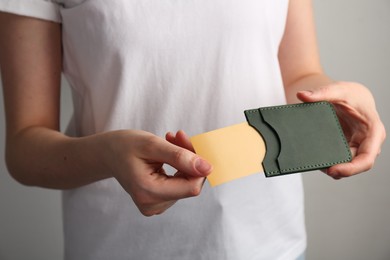 Woman holding leather business card holder with card on grey background, closeup