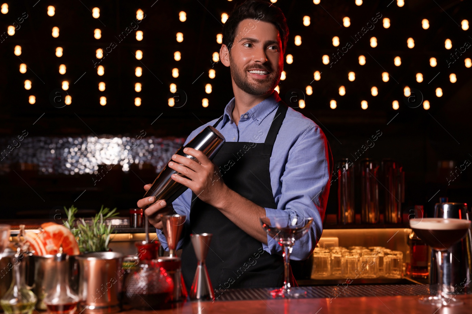 Photo of Bartender with shaker preparing fresh alcoholic cocktail in bar