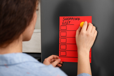 Photo of Woman putting shopping list on refrigerator door, closeup