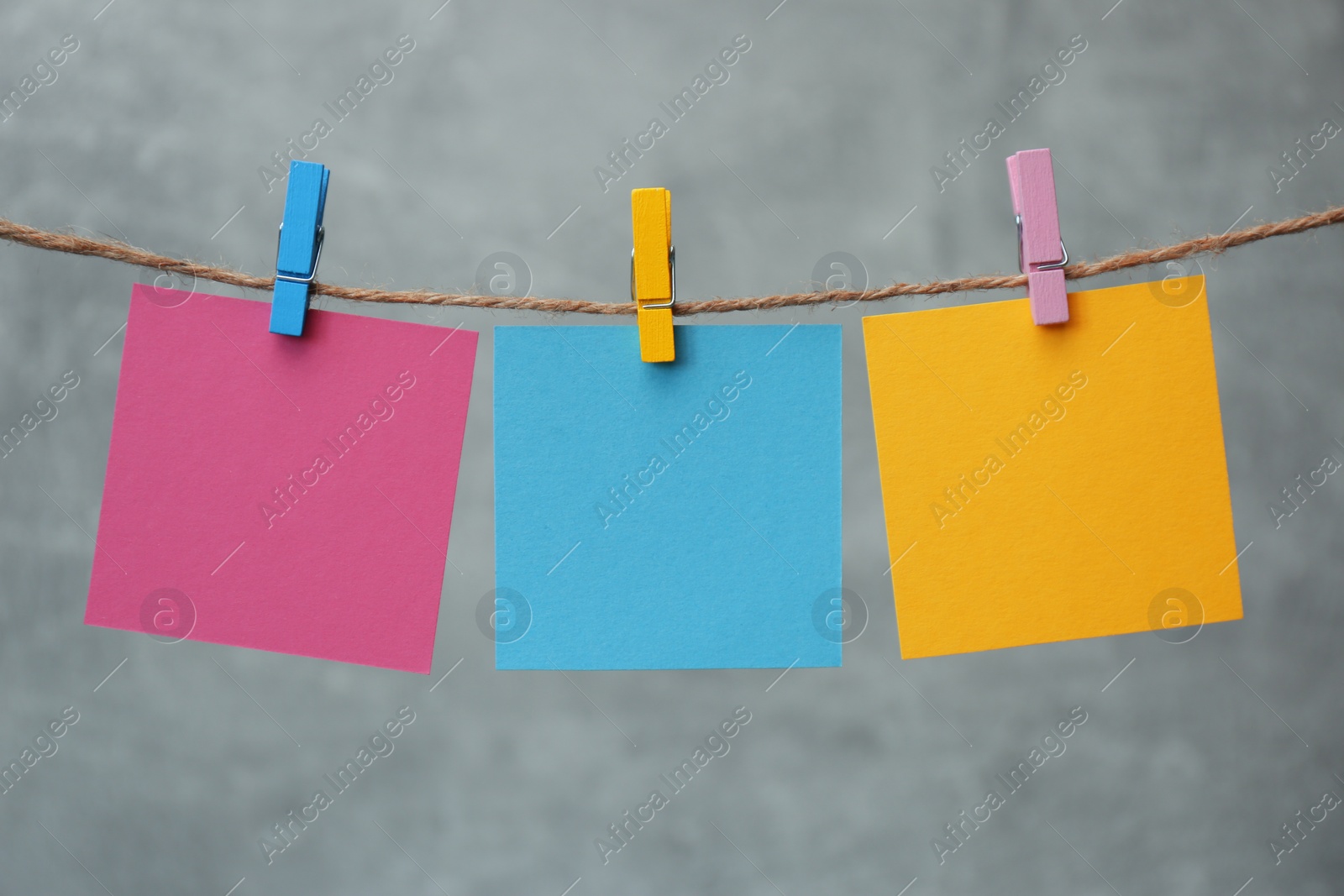 Photo of Wooden clothespins with colorful blank notepapers on twine against marble background. Space for text