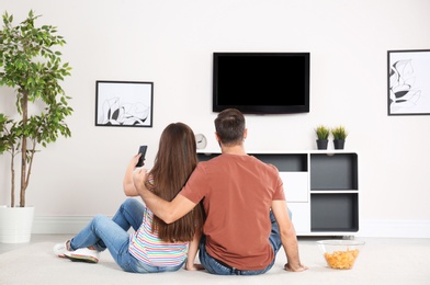 Photo of Young couple sitting on floor and watching TV at home