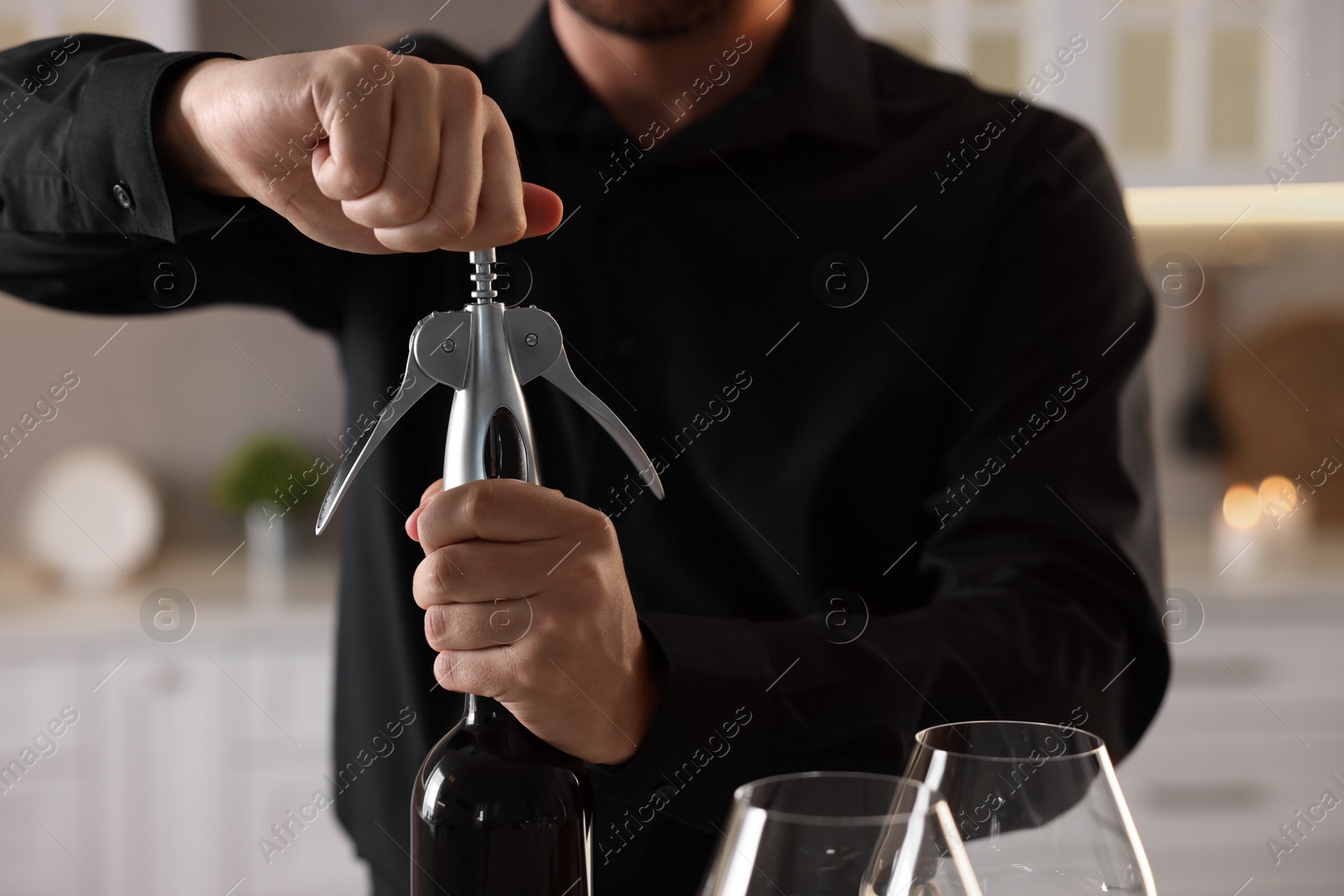 Photo of Man opening wine bottle with corkscrew indoors, closeup