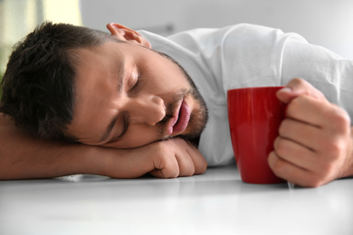 Man with cup of drink sleeping at home in morning