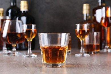 Photo of One liqueur in glass in front of others on grey textured table, closeup