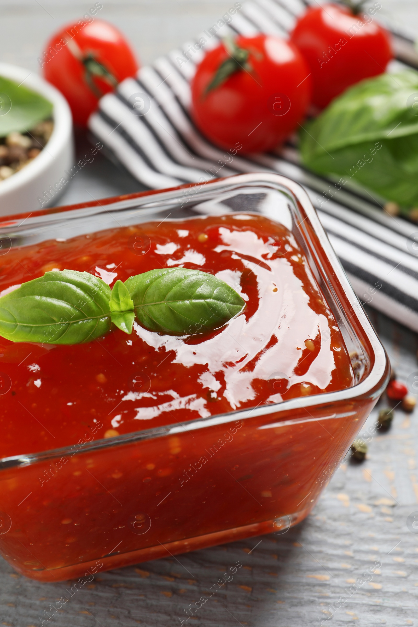 Photo of Spicy chili sauce with basil on grey wooden table, closeup