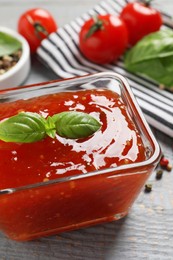 Photo of Spicy chili sauce with basil on grey wooden table, closeup