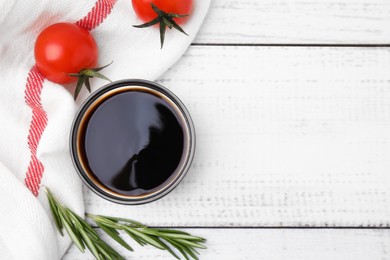 Photo of Bowl with balsamic vinegar, rosemary and tomatoes on white wooden table, flat lay. Space for text