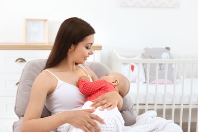 Young mother with her cute baby girl in armchair at home